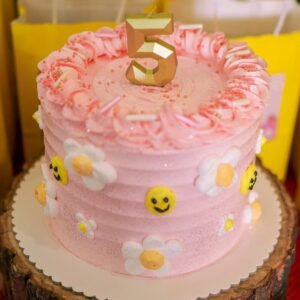 Vibrant pink birthday cake with cheerful emoji and flower decorations, surrounded by party gift bags.