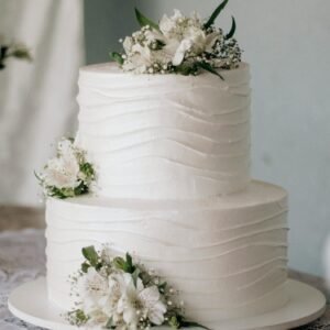 Beautiful two-tier white wedding cake adorned with fresh flowers on a rustic wooden table.