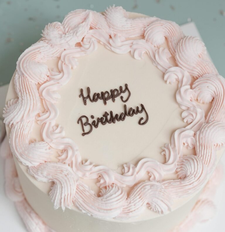 Top view of a white birthday cake with pink frosting decorations and 'Happy Birthday' text.