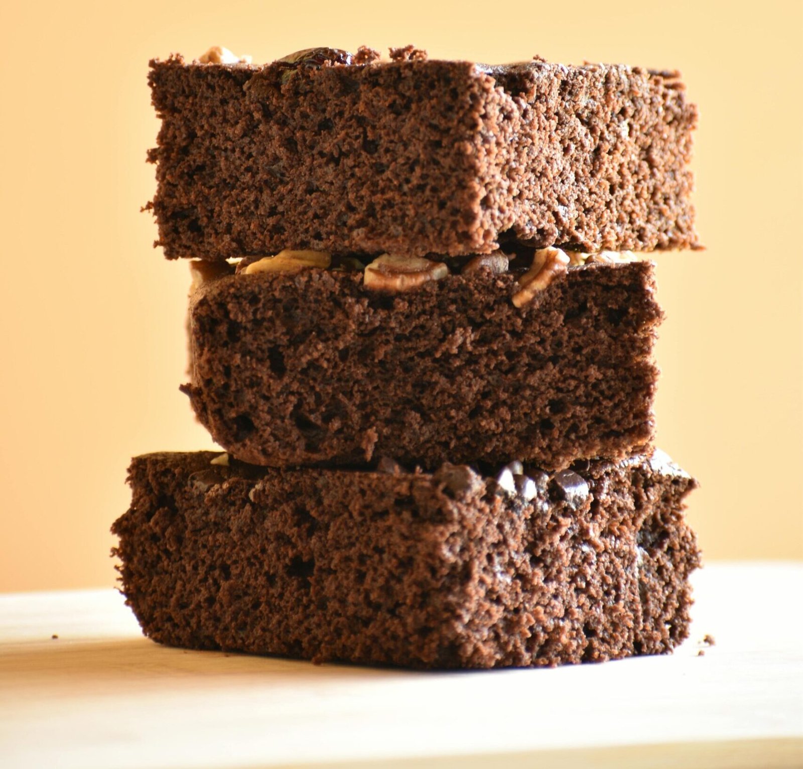 Three pieces of rich homemade chocolate brownies stacked on a wooden surface.